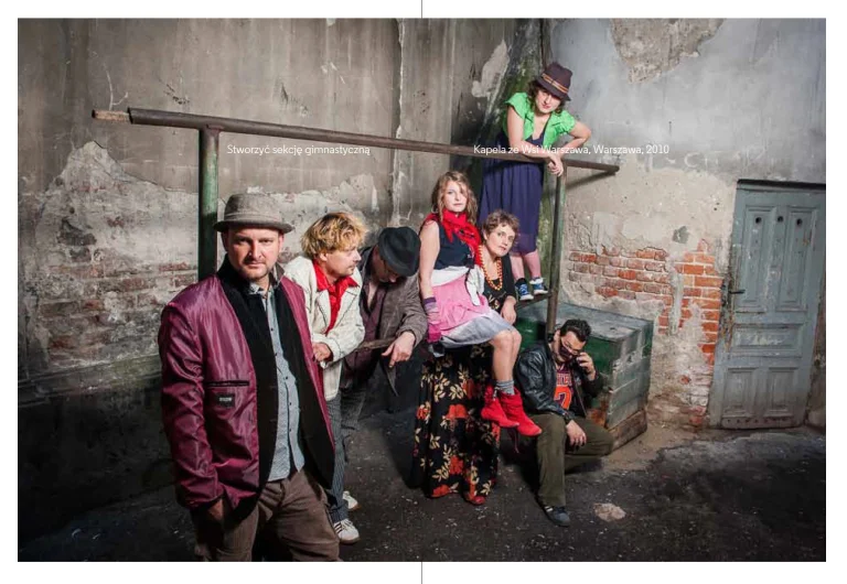 Zdjęcie zespołu Kapela ze Wsi Warszawa z albumu fotograficznego '10 Lat Karrot'. Przedstawia ubrany na kolorowo zespół na podwórku na tle metalowego trzepaka.